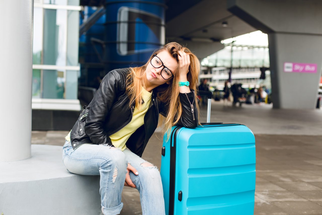 portrait-pretty-girl-with-long-hair-glasses-sitting-outside-airport-she-wears-yellow-sweater-with-black-jacket-jeans-she-leaned-suitcase-is-bored-waiting-1280x853.jpg